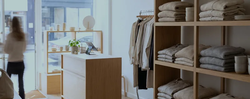 A bright boutique clothing shop with folded knitwear on wood shelving