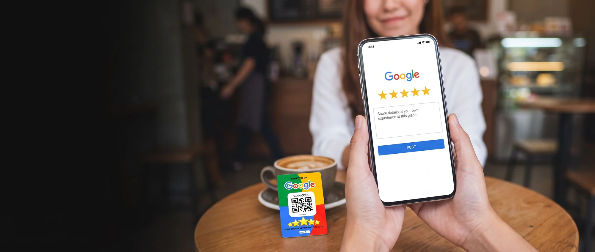A solo customer at a cafe window table holding up a phone to a five-star Google review page, with a Tapping Tags review card resting beside her coffee cup