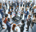 A diverse group of professionals forms a circle around a central digital device emitting icons, suggesting a tech conference or networking event.